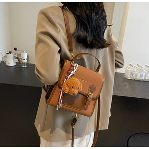 Detail of brown faux leather crossbody bag with plush dog charm and red plaid scarf