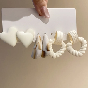 Detailed close-up of acrylic C-shaped earrings in white heart and marbled brown patterns