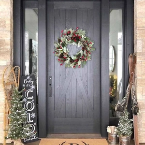 Close-up of Christmas wreath with red berries and pine cones on a dark grey wooden door