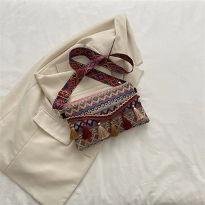 Detail of woven bohemian envelope bag with colorful tassels and geometric strap