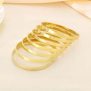 Close-up of seven stacked minimalist gold titanium steel bangles with polished finish