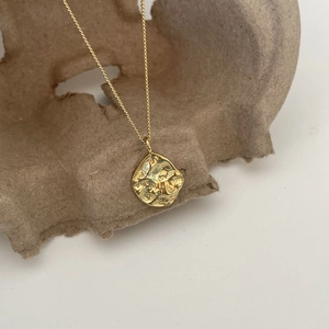 Detail of golden irregular round pendant with hammer texture on a rustic display stand