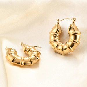 Close-up of chunky gold croissant hoop earrings on elegant beige silk background