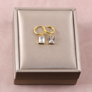Detalle de pendientes de circonio dorado rectangular sobre un joyero de terciopelo rosa