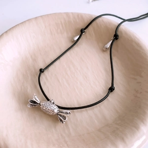 Detail of candy-shaped metal pendant with vintage texture on a black woven cord necklace