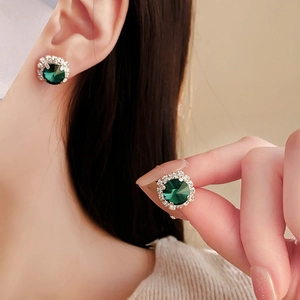 Close-up of circular green crystal stud earrings with sparkling diamond halo on model