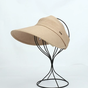 Detail of beige wide brim sun visor showing breathable woven texture and metal logo