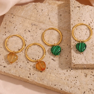 Gold heart drop earrings featuring natural orange and green stone charms on stone surface