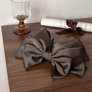 Detail of a large dark brown satin bow hair clip on a premium wooden background