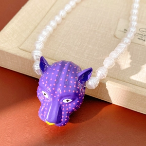 Détail d'un pendentif tête de panthère violette à pois roses sur un collier de perles