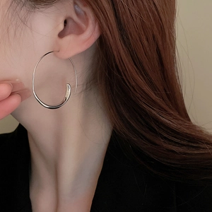 Close-up of a large silver geometric hoop earring with polished finish on a model
