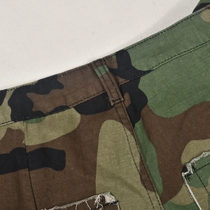 Détail macro du short en denim camouflage avec passants de ceinture et poches effilochées
