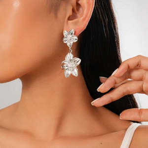 Detailed view of silver flower statement earrings with metallic texture on model's ear