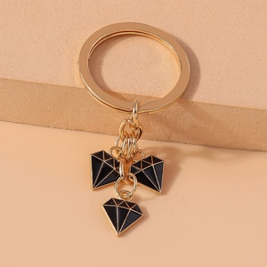 Detail of gold metal keychain with black enamel diamond charms on textured background