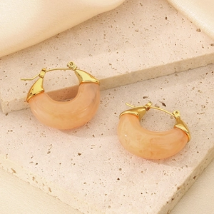 Macro detail of U-shaped orange resin hoop earring on a beige stone surface