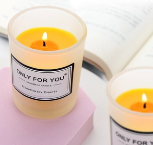 Close-up of a handmade aromatherapy candle in a frosted glass jar on a purple pedestal