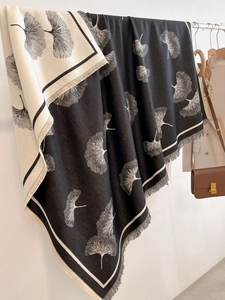 Detail of double-sided ginkgo leaf pattern scarf with tassels hanging on a hanger