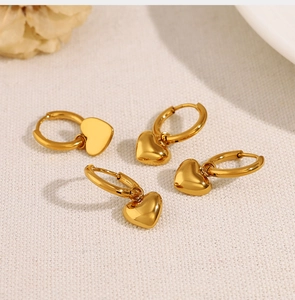 Close-up of elegant gold heart dangle earrings on a beige textured fabric background