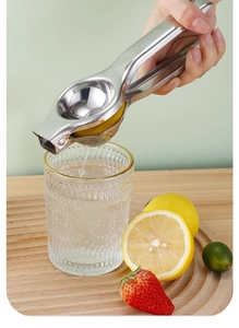 Manual stainless steel lemon squeezer pressing fresh juice into a glass over a wooden board