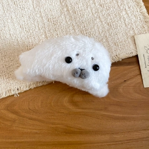 Detail of soft white plush seal hair claw clip with black eyes on a beige woven mat