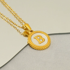 Macro view of golden letter B pendant with white inlay on a reflective mirror surface