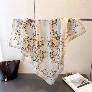 Vue détaillée du foulard carré en soie avec imprimés floraux orange et bordure dorée fine