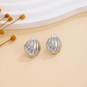 Detailed close-up of silver textured shell-shaped earrings on a beige background