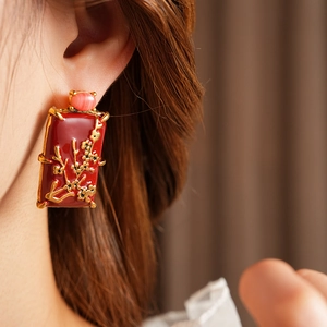 Détail d'une boucle d'oreille vintage en émail rouge avec motif floral doré sur le modèle