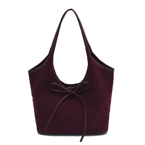 Detailed close-up of a burgundy suede shoulder bag featuring a decorative bow element
