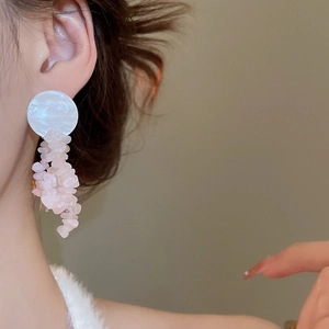 Close-up of pink crystal tassel earrings with white shell studs worn by a model
