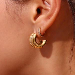 Detail of gold double C-shaped earrings with one smooth and one zircon studded band