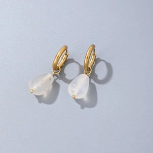 Detailed view of teardrop natural stone earrings with polished gold rings and white pendants