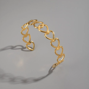 Detailed view of hollow heart-shaped gold-plated stainless steel cuff with artistic shadow