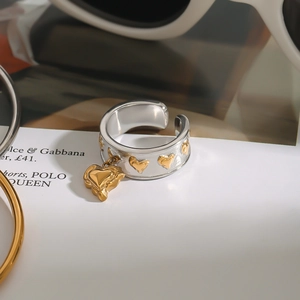 Detail of wide open steel ring with golden heart reliefs and a hanging heart charm