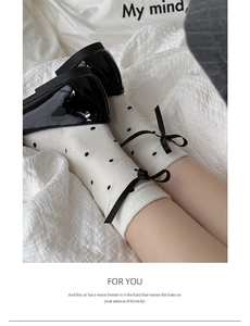 Detail of white cotton mid-calf socks with black polka dots and side ribbon bow accents