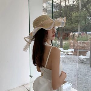 Detail of woven sun hat featuring elegant pearl accents and wavy mesh brim for beach vacation