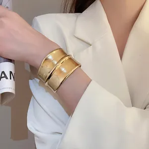 Bracelet manchette large plaqué or au design ondulé minimaliste porté par un mannequin
