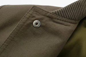 Macro detail of olive green canvas fabric with silver metal snap button and rib-knit cuff