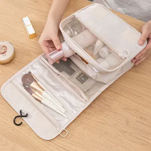 Hanging toiletry bag with mesh dividers and metal hook on a light wood surface