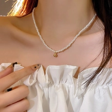 Detail of beaded pearl necklace featuring a central golden spherical pendant on model