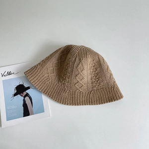 Detail of caramel cable knit bucket hat with textured patterns on a neutral background