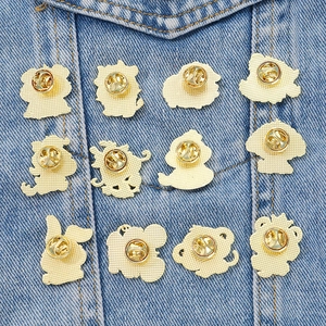 Set of 12 gold metal Chinese zodiac animal brooches on denim background with butterfly clasps