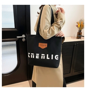 Close-up of black canvas tote bag with ENERLIG lettering worn with a beige trench coat
