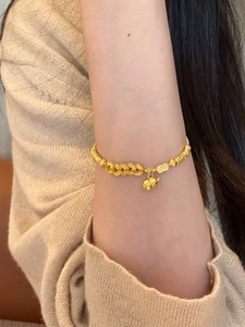Detailed close-up of a gold-plated gourd charm bracelet worn on a female wrist