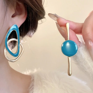 Close-up of asymmetrical geometric earrings with bright blue enamel and gold finish