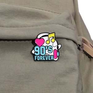 Gros plan d'un pin's en émail 90'S FOREVER avec cœur et écouteurs fixé sur un sac à dos
