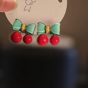 Close-up of cherry bow earrings featuring red beads and green translucent bows