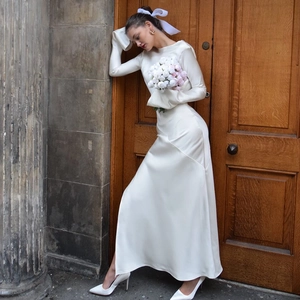 Detail of elegant white satin long-sleeve dress with back bow and slit in classical setting