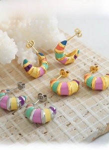 Close-up of vintage C-shaped striped enamel earrings in colorful pastel shades on coral