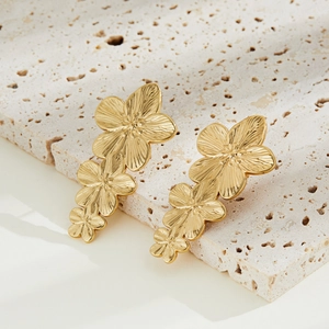 Detailed macro view of three layered gold floral earrings on a natural stone surface